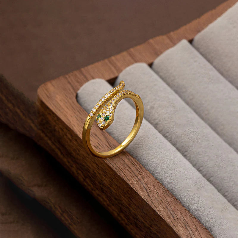 Gold snake-shaped ring with green gemstones on a wooden jewelry display.