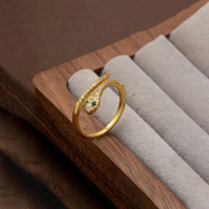 Gold snake-shaped ring with green gemstones on a wooden jewelry display.