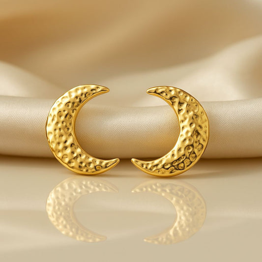 Gold crescent moon earrings on a beige fabric background