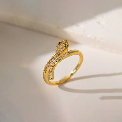 Gold snake-shaped ring with green and clear gemstones on a light background